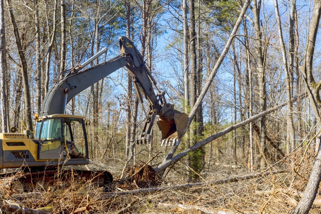 Worker removing trees from forests, preparing ground for building house, using an excavator